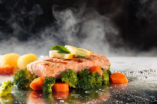 Salmon steak and steamed vegetables on tray with steam.