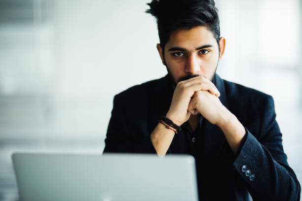 istock Indian thinking Man in glasses working on laptop in modern office 954602314