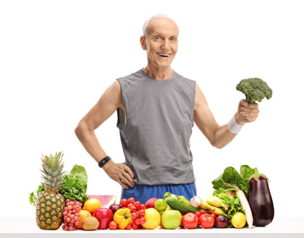 istock Senior behind a table with fruit and vegetables holding broccoli 954611240