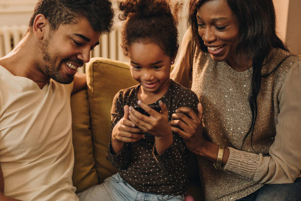 istock Happy African American girl and her parents having fun while using smart phone. 954617122