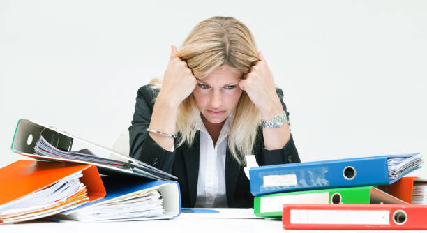 istock Female white collar worker sitting with headache at table with ring binders 954625156
