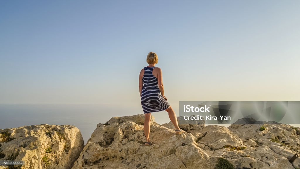 Middle-aged woman looks into distance Blonde middle-aged woman in blue dress greets the sun dawn looks into distance and enjoying life , summer concept Active Lifestyle Stock Photo