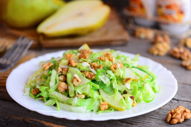 istock Pear cabbage slaw salad. Homemade salad with fresh pear, cabbage and walnuts on a white plate and on rustic wooden background. Comfort food lunch recipe. Cooking light diet. Closeup 954649578