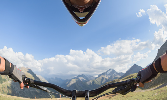 Mountain bike handlebar controlled by male biker in staggering alpine scenery on a sunny day