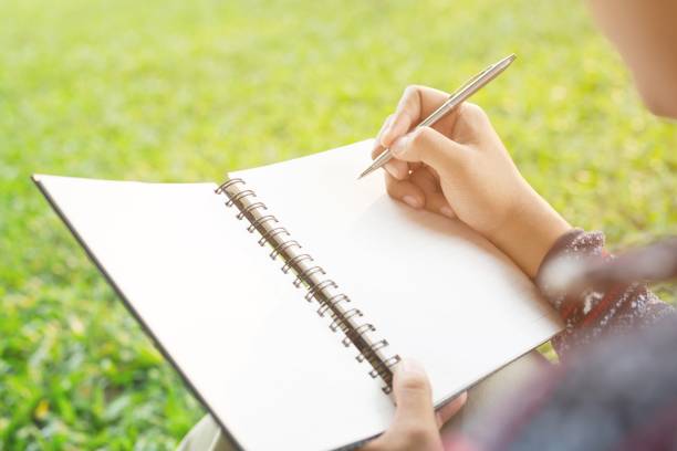 istock close up hand young man are sitting using pen writing Record Lecture notepad into the book in the parks. 954681404