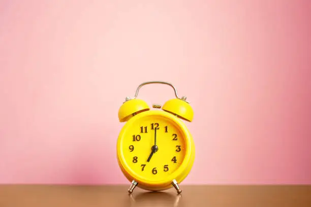 Photo of yellow alarm clock seven o'clock in the morning on the table against the pink wall. time for people to get to work, for kids to school