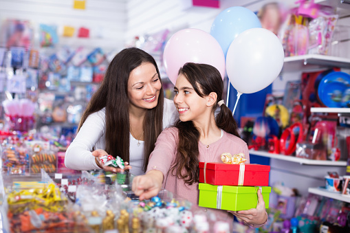 Smiling cheerful positive female and girl with gifts and balloons in the candy store