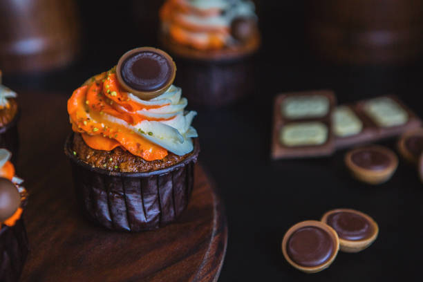 istock Cupcakes with orange-and-white cream in a dark glass, decorated with chocolate, biscuits and sweets 954706010
