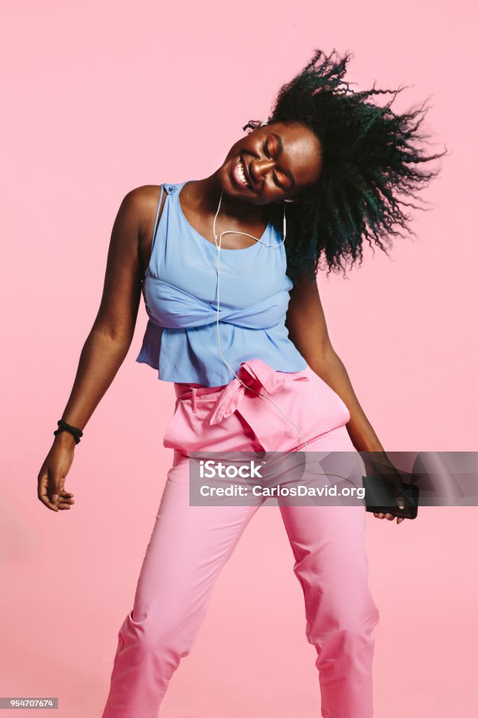 Girl dancing and listening to music on earphones A young African American girl dancing, smiling, and listening to music on her headphones, holding cell phone with hair up in the air and eyes closed Dancing Stock Photo