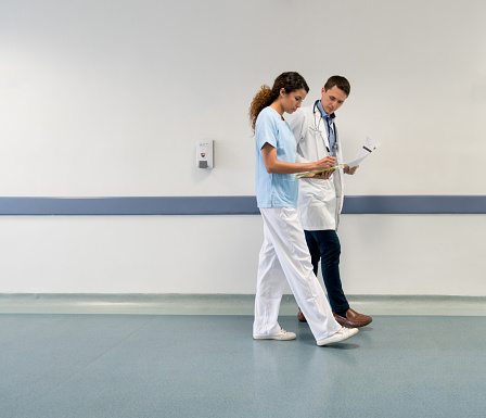 Nurse and doctor walking down the corridor while looking at a patients medical chart very focused