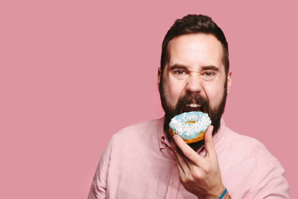 Man holding blue donut and taking a big bite A man with beard looking at camera about to take a big bite of a blue donut he is holding in his hand hedgehog mushroom stock pictures, royalty-free photos & images