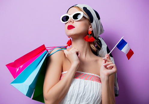 Portrait of beautiful style woman in sunglasses with french flag and shopping bags on purple background