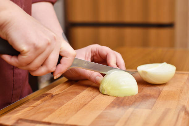 istock Female hands using a knife cut a fresh onion on a cutting board 954732382