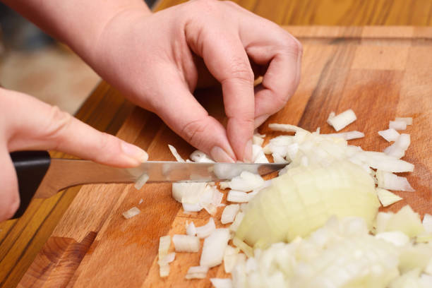 istock Female hands using a knife cut a fresh onion on a cutting board 954732436