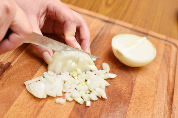 istock Female hands using a knife cut a fresh onion on a cutting board 954732726