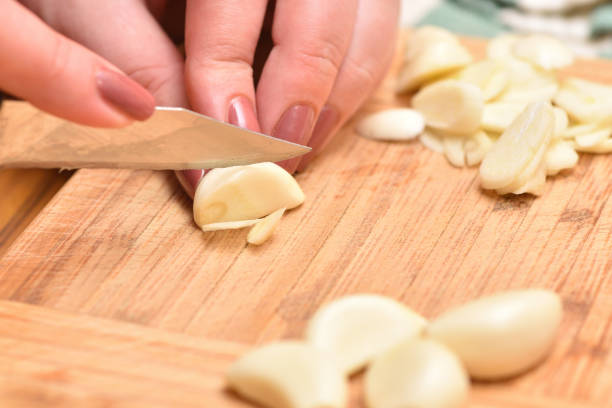 istock Female hands with a knife chop fresh garlic on a cutting board 954732848