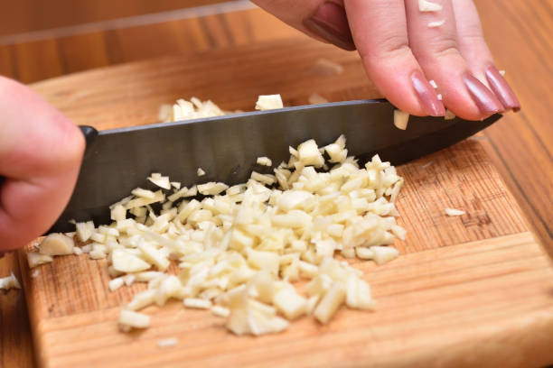 Female hands with a knife chop fresh garlic on a cutting board stock photo