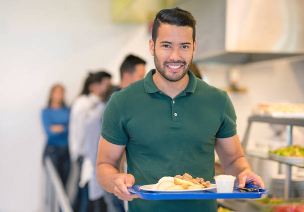 istock Cheerful young fit man holding his tray at a buffet looking at camera smiling 954735532