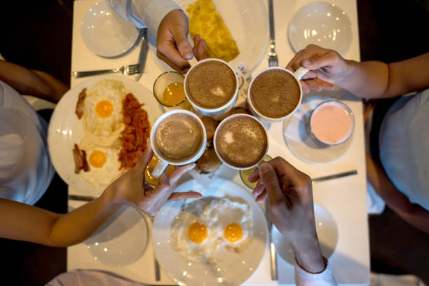 Group of unrecognizable people eating breakfast enjoying eggs and other foods and toasting with hot chocolate
