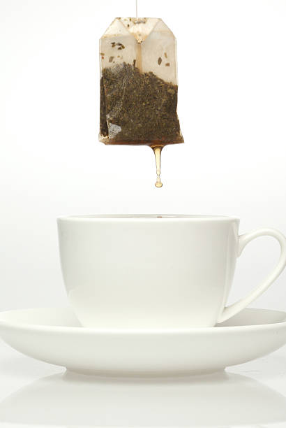 Teabag dripping over white cup and saucer stock photo