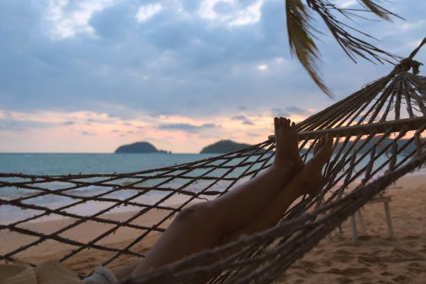 Summer vacations concept, Happy woman legs with hat and shorts Jeans relaxing in hammock on tropical beach at sunset, Koh mak, Thailand