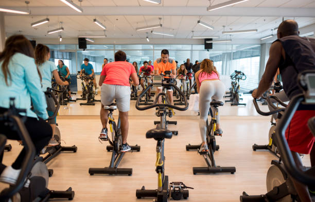 istruttore maschile nell'esercizio della lezione e tutti coloro che lo seguono - spinning instructor exercising gym foto e immagini stock