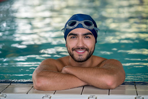 Portrait of latin american male swimmer leaning at the edge of the pool looking at camera smiling very happy