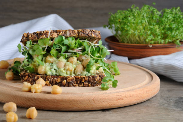 Sandwich of rye bread with cereals with crushed avocado, chickpeas and sprouts of radish shoots. stock photo
