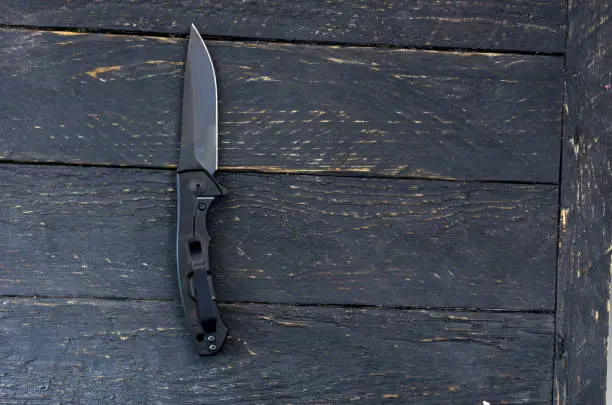 Photo of Black knife with a black blade. Dark wooden background.