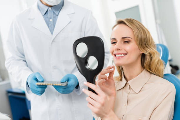 donna che sceglie l'impianto dentale guardando lo specchio nella moderna clinica dentale - impianto dentale foto e immagini stock