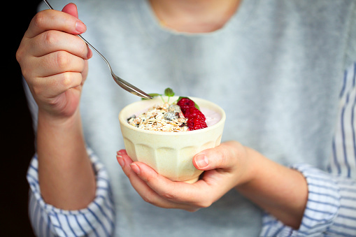 Healthy breakfast greek yogurt, granola and raspberries in the bowl in hands of woman
