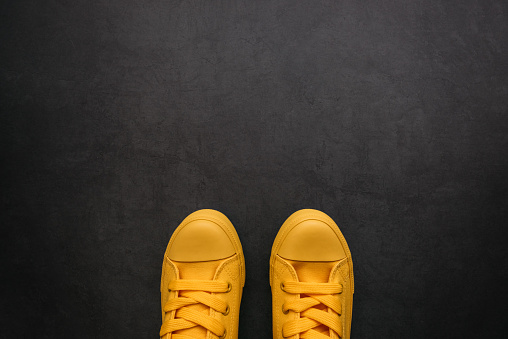 Stylish yellow sneakers on dark background with copy space, top view