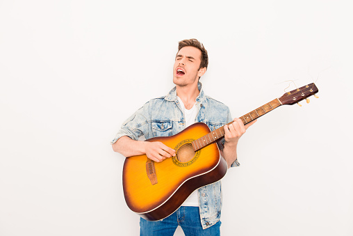 Young musician playing on guitar and singing on white background