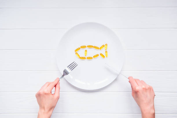 Top view female hands holding knife and fork under round plate with Cod Liver Oil Capsules, Omega 3, Vitamin D in the fish shape on the white wooden table. Selective focus, space for text vista superior femenina manos sosteniendo el cuchillo y el tenedor debajo de placa redonda con cápsulas de aceite de hígado de bacalao, omega 3, vitamina d en los pescados de la forma en la mesa de madera blanca. enfoque selectivo, espacio para texto.