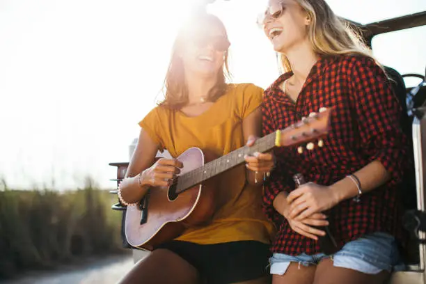 Two girlfriends enjoying 
 summer day outdoors playing a guitar