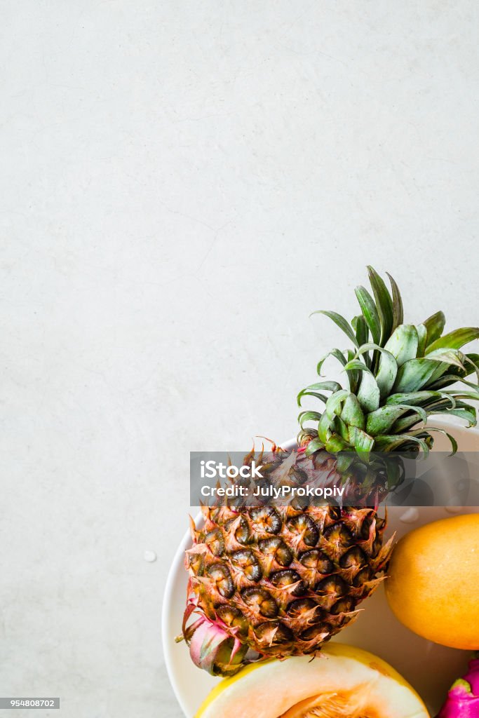 Pineapple and melon fruits, minimal food photo Pineapple and melon fruits on a white plate, gray concrete background. Creative layout, minimalist food photography concept. Copyspace, vertical Above Stock Photo