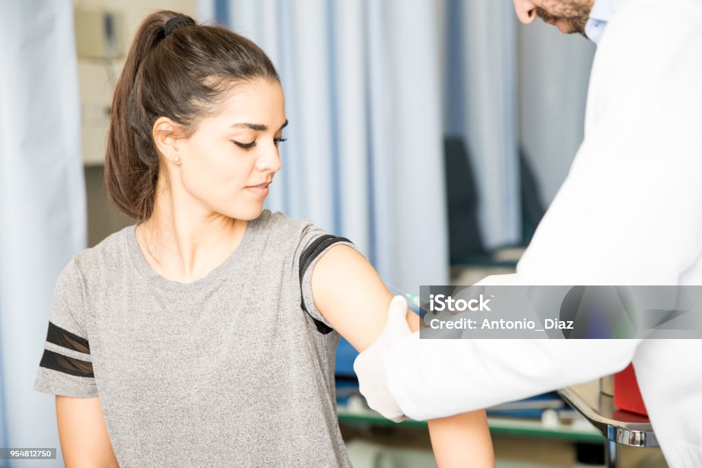 Woman patient getting vaccinated Attractive hispanic female patient getting vaccine on her arm by a doctor in hospital Vaccination Stock Photo