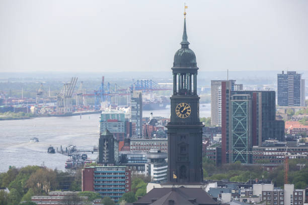 Panoramic aerial view over the rooftops of Hamburg, from the copper tower of Hauptkirche Sankt Michaelis, St Michael’s Church, past the high rises of St. Pauli to the busy cranes of the Port of Hamburg and blue waters of the Elbe, Germany.