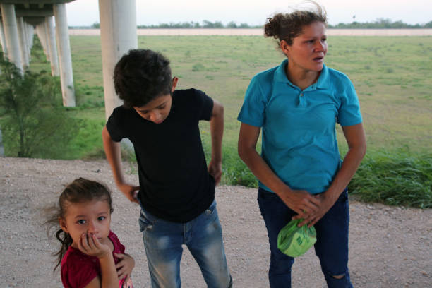 August 16, 2017 - McAllen, Texas, USA - A young Honduran woman and her two children who had just crossed the Rio Grande River wait to be taken into custody by Border Patrol agents and ask for asylum.  A steady stream of Central Americans, ranging from single children to entire families fleeing gang violence, continue to make the dangerous journey across Mexico to the U.S.