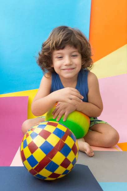 Little happy boy playing with multi colored balls.Cute baby boy playing with balls on colorful background