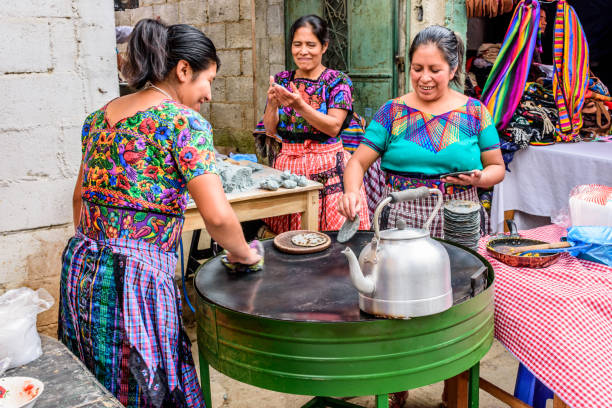 Local women make tortillas in the street, Santiago Sacatepequez, Guatemala Local Maya women dressed in traditional clothing make corn tortillas in the street during the giant kite festival on All Saints' Day. experiential travel stock pictures, royalty-free photos & images