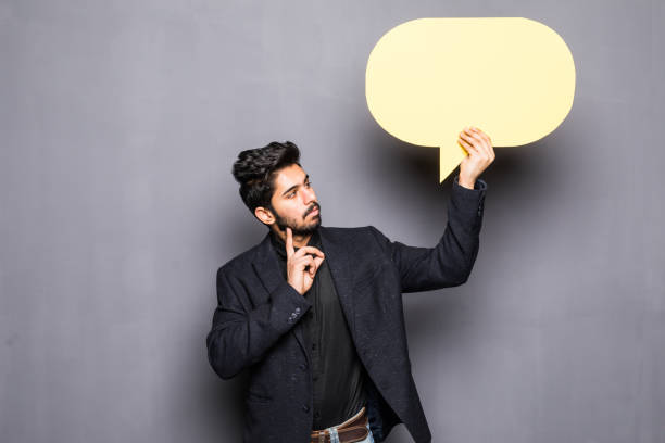 istock Young indian business man holding a bubble for text, isolated on a grey background 954833982