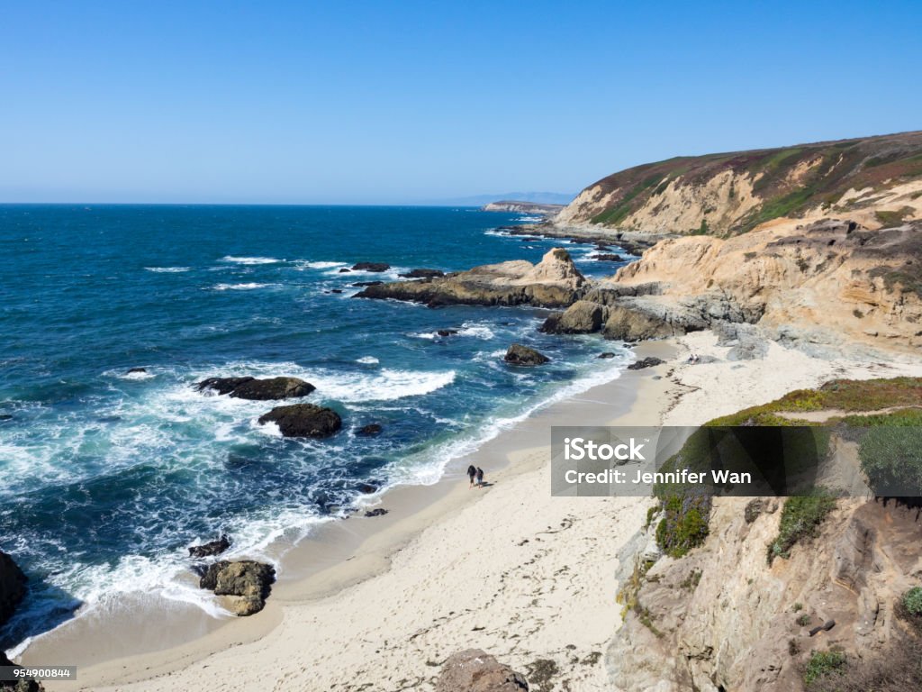 Barefoot hikers on beach below rocky cliffs and waves along shore in Bodea Head, Marin County, California, United States Bodega Bay Stock Photo