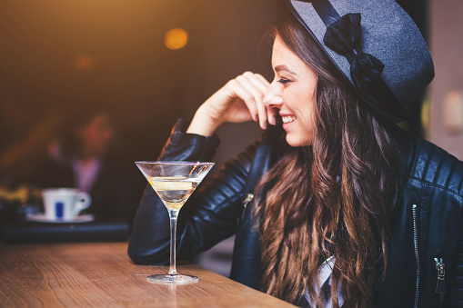 Young brunette woman sitting at a bar and enjoying a cocktail with a lemon twist.