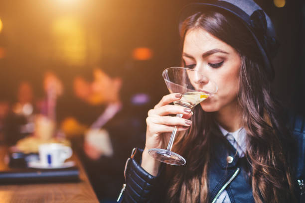Young brunette woman sitting at a bar and enjoying a cocktail with a lemon twist.