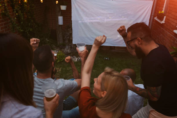 istock Friends Watching Soccer Game On Big Screen In Backyard 954927320