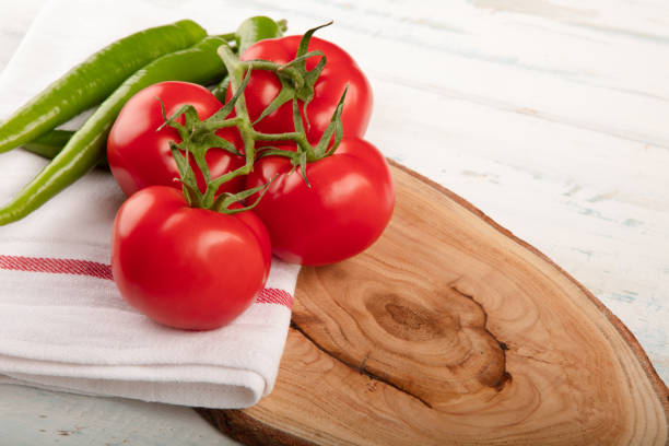Natural ripe tomatoes branch and several green pepper on a wooden plate with copy space