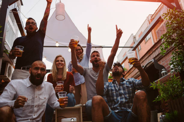 Friends Watching Sports On Big Screen In Backyard