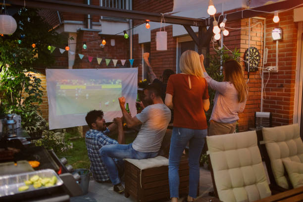 Friends Watching Sports On Big Screen In Backyard