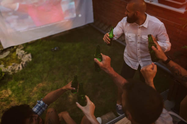 amis, regarder les sports sur grand écran dans l’arrière-cour - barbecue foot photos et images de collection